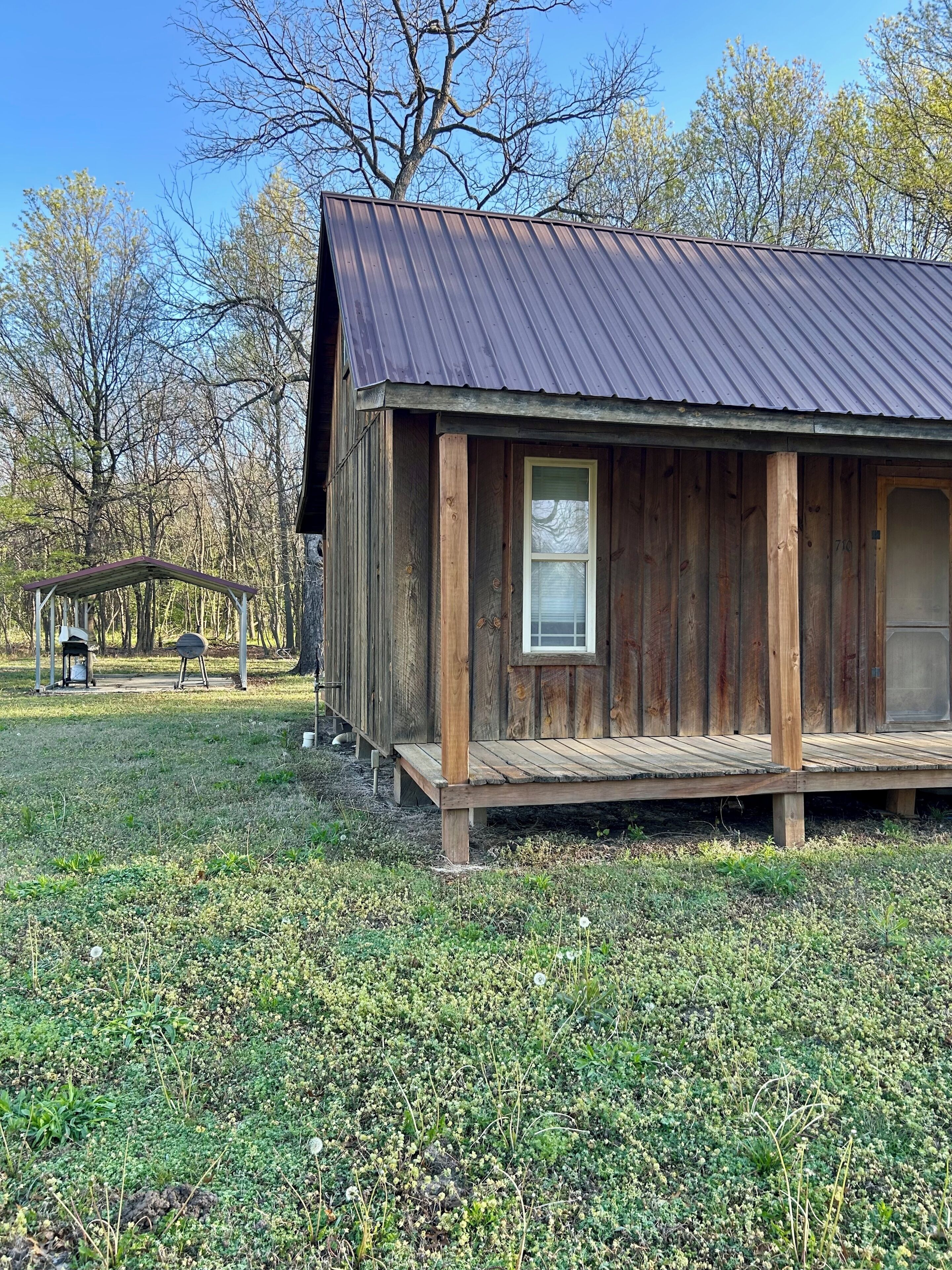 A rustic wooden cabin with a metal roof, a porch, and a small window.