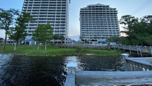 Twee hoge gebouwen met balkons, een houten steiger en een wateroppervlak.