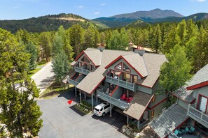 A two-story building with a balcony, a car parked in front, and a mountainous landscape in the background. - NEW! Pine Creek Townhome, Private Hot Tub & Garage (Breckenridge)