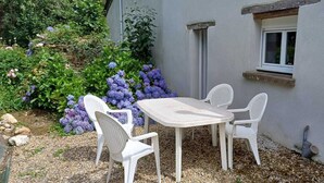 Un patio con una mesa y cuatro sillas, rodeado de un jardín con flores moradas.