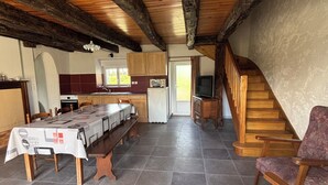 Un comedor amplio con una mesa larga, sillas de madera, una cocina con armarios y una escalera que lleva a un nivel superior.