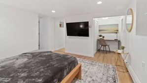 A bedroom with a bed, a desk, a chair, a TV, and a mirror.