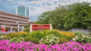 A welcome sign to Stamford Downtown with a building in the background.