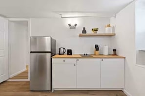 A modern kitchen with white cabinetry, a stainless steel refrigerator, a wooden countertop, and a wall-mounted shelf with kitchen items.