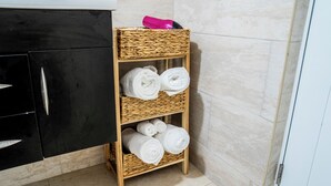 Een badkamer met een zwart kastje, een rieten plank met handdoeken, en een roze fles.