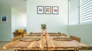 Een eetruimte met een houten tafel, stoelen, een vaas met planten en lijstjes met foto's aan de muur.