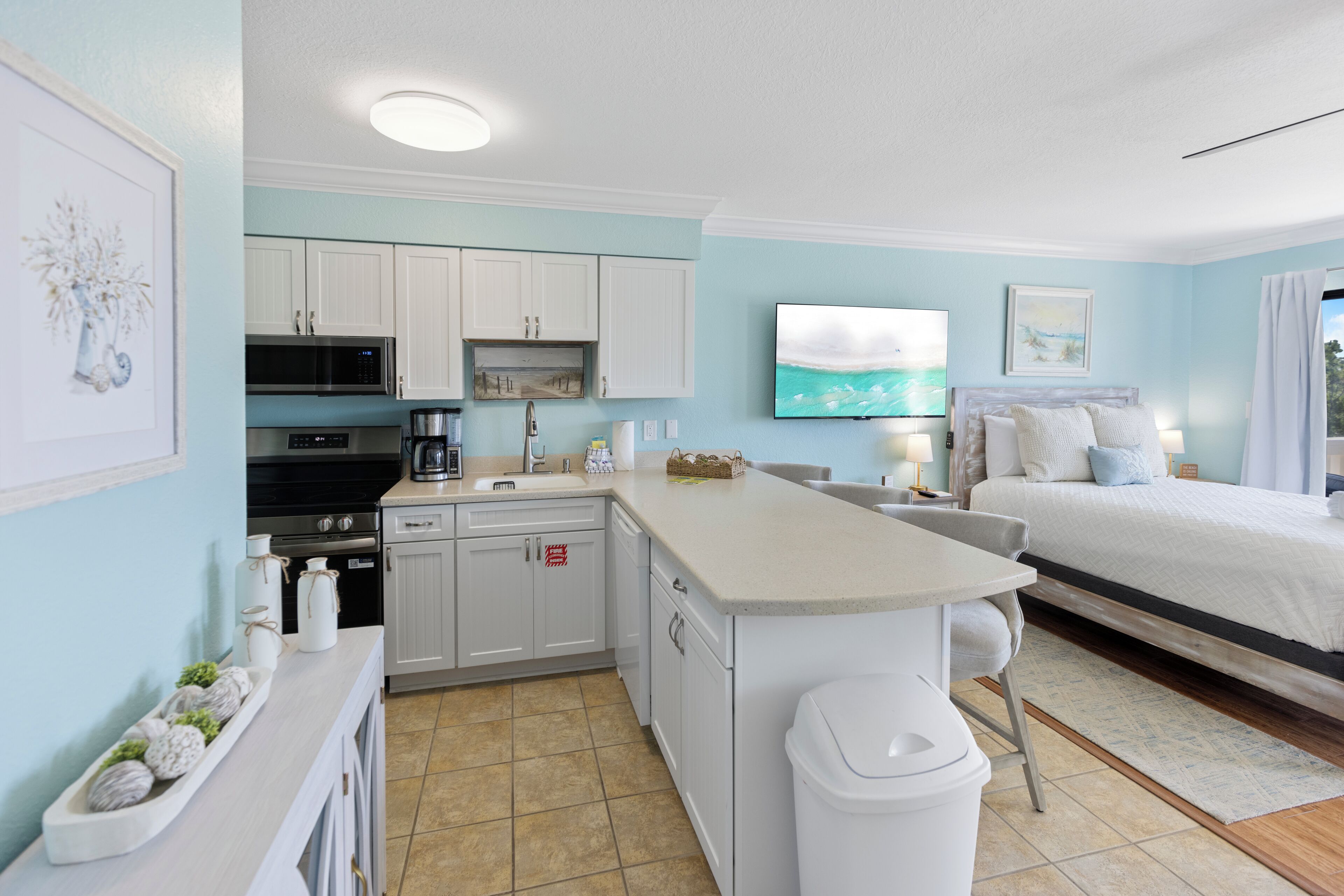 Une chambre d’hôtel de taille réduite, équipée d’une kitchenette, d’un lit, d’une télévision et d’une salle de bain.