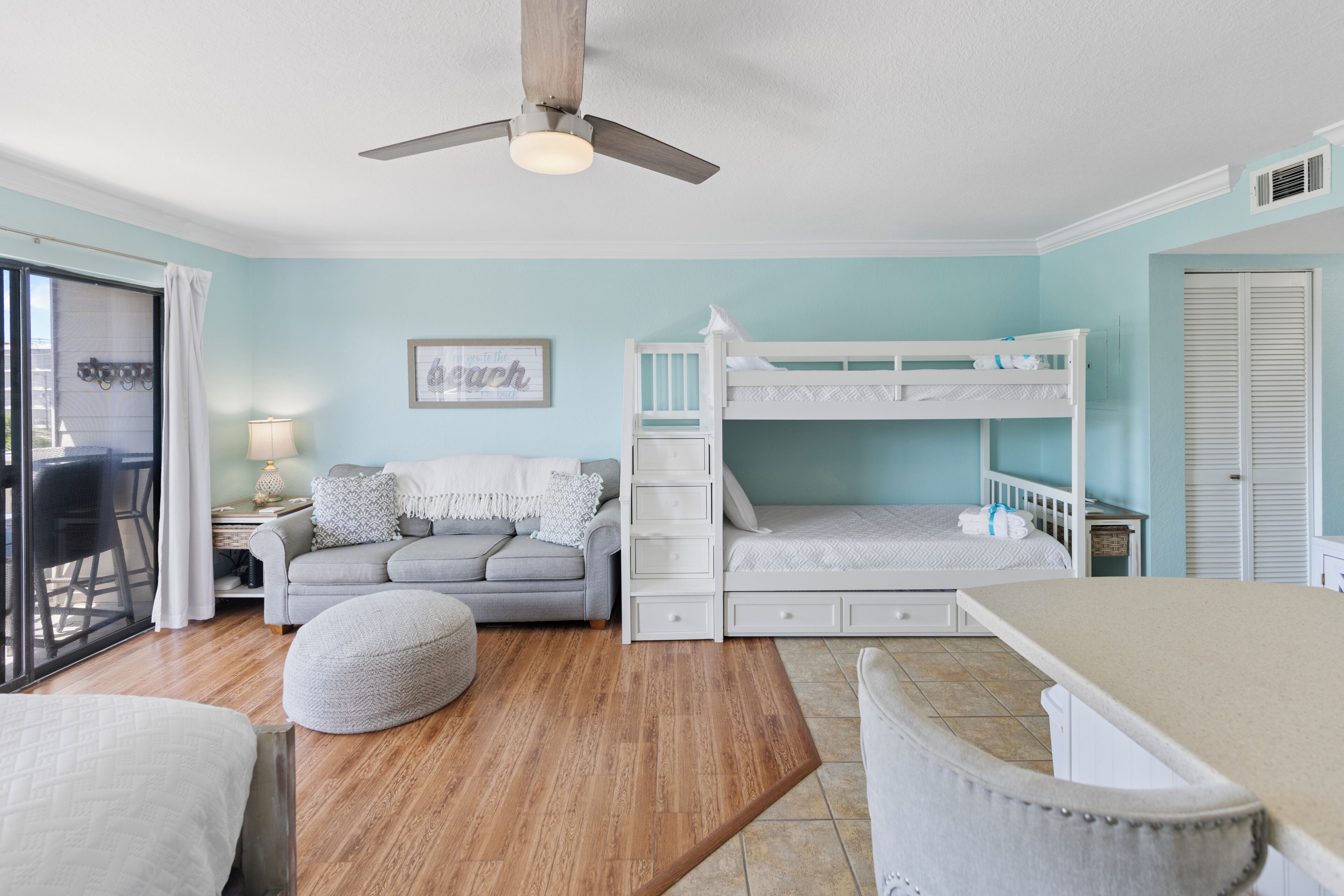 A room with a bunk bed, a sofa, a dining table, and a ceiling fan.