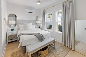 Ein Schlafzimmer mit Bett, Nachttischen, einem Spiegel, einem Fenster mit Vorhängen und einem Deckenventilator.