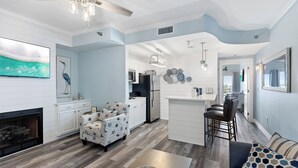 Una cocina moderna con armarios blancos, una zona de comedor con taburetes de bar y una sala de estar con sofá y sillón estampado.