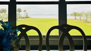 Quarto com uma janela grande com vista para uma área gramada e um corpo de água. Há duas cadeiras em primeiro plano.