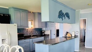 Uma cozinha com armários azuis, uma ilha central e um espaço de jantar com cadeiras brancas.