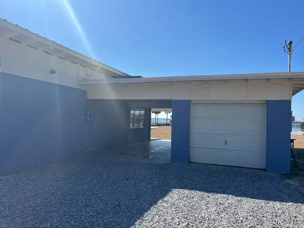 Eine Garage mit Wohntrakt, Kiesauffahrt und freiem Blick auf den Strand im Hintergrund.