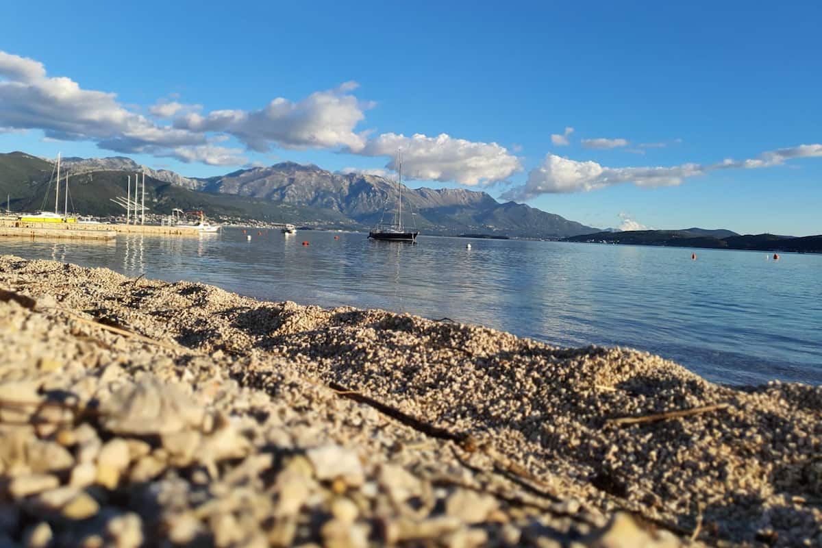 Ein Kiesstrand mit Booten, blauem Himmel und Bergen im Hintergrund.