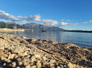 A pebbly beach with boats, a clear sky, and mountains in the background. - Comfort Accommodation Baošići Montenegro (Baošići)