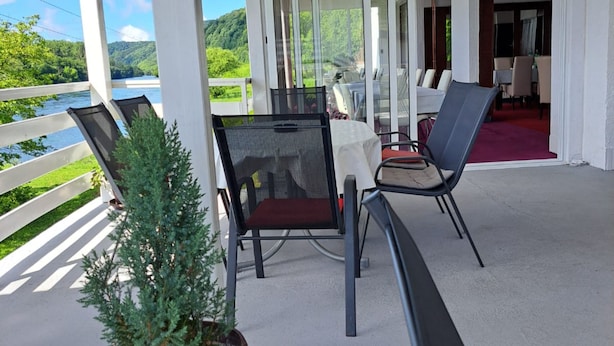A covered outdoor seating area with a table and chairs, a potted plant, and a view of a river and hills.