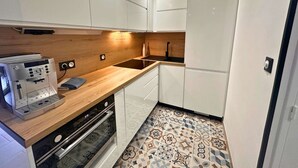 A compact kitchen with white cabinets, a wooden countertop, a built-in oven, and a patterned tile floor. - Asteria by Pom, pkg, clim, wifi (Agde)