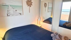 A bedroom with a bed, a nightstand, a lamp, a mirror, and artwork on the wall. - Asteria by Pom, pkg, clim, wifi (Agde)