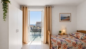 A bedroom with a bed, a nightstand, a lamp, a framed picture, and a view of the balcony.