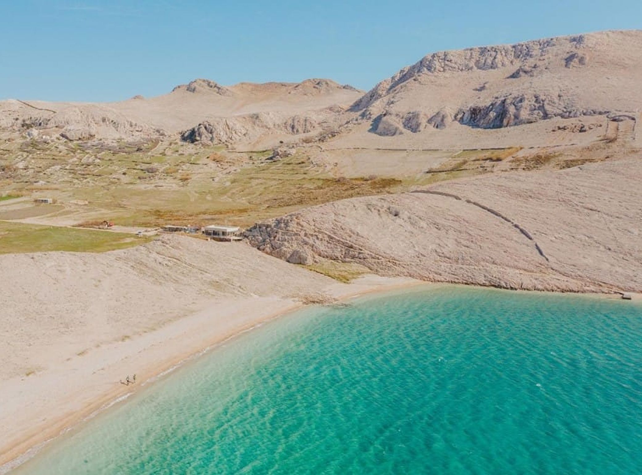 Eine Küstenlandschaft mit klarem türkisblauem Wasser, felsigem Gelände und einem kleinen Gebäude.