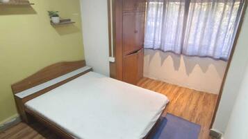 A small bedroom with a bed, a wooden floor, a ceiling fan, and a door leading to another room.