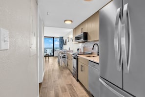 A modern kitchen with stainless steel appliances, wooden cabinets, and a view to the outside. - Compass Cove 1466: Beach View (Myrtle Beach)
