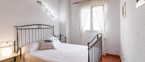 A bedroom with a bed, bedside lamp, window with curtains, and a wooden ceiling.