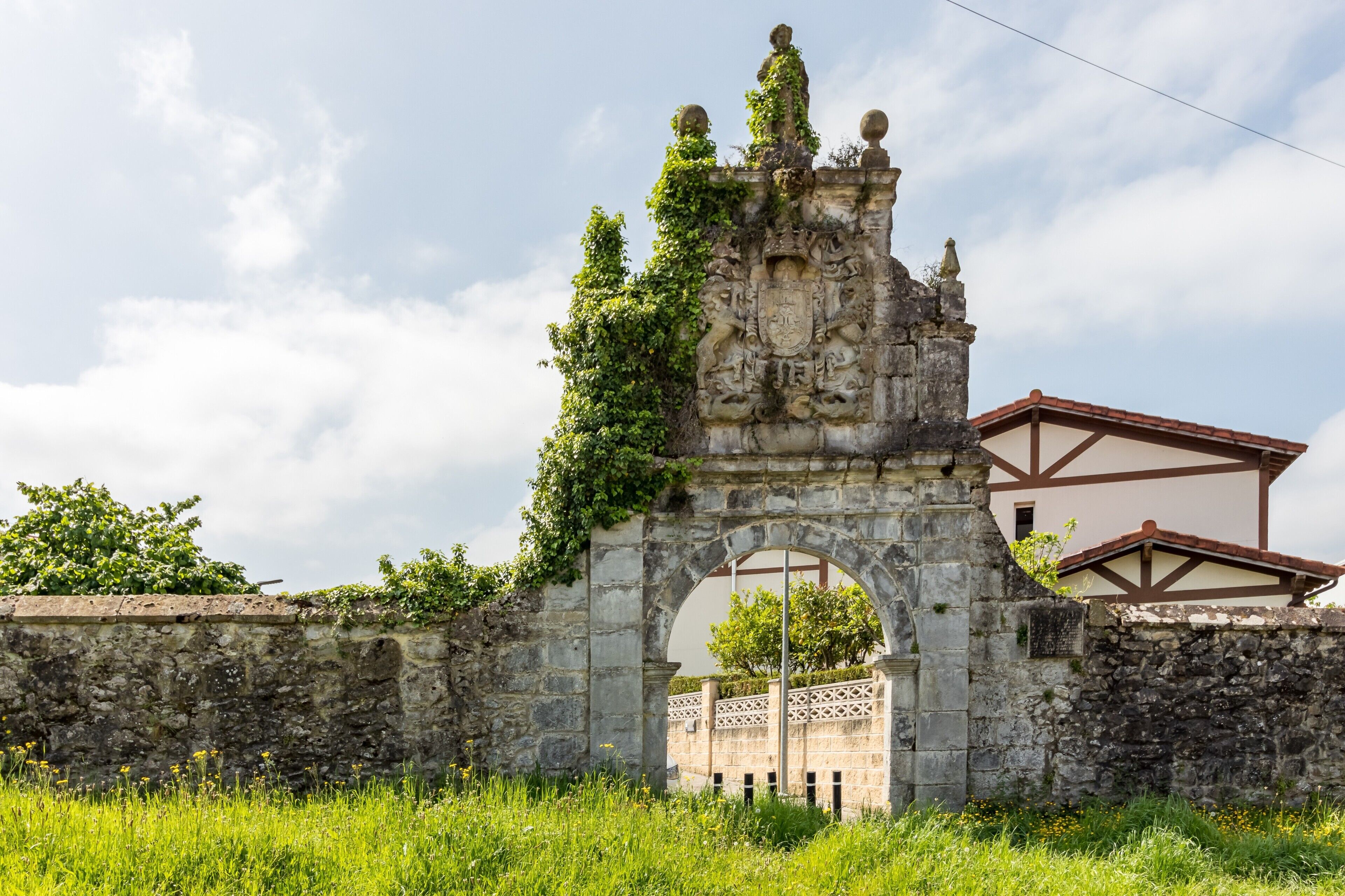 Un vieux portail en pierre, orné de sculptures complexes, et un bâtiment avec un toit recouvert de tuiles rouges en arrière-plan.