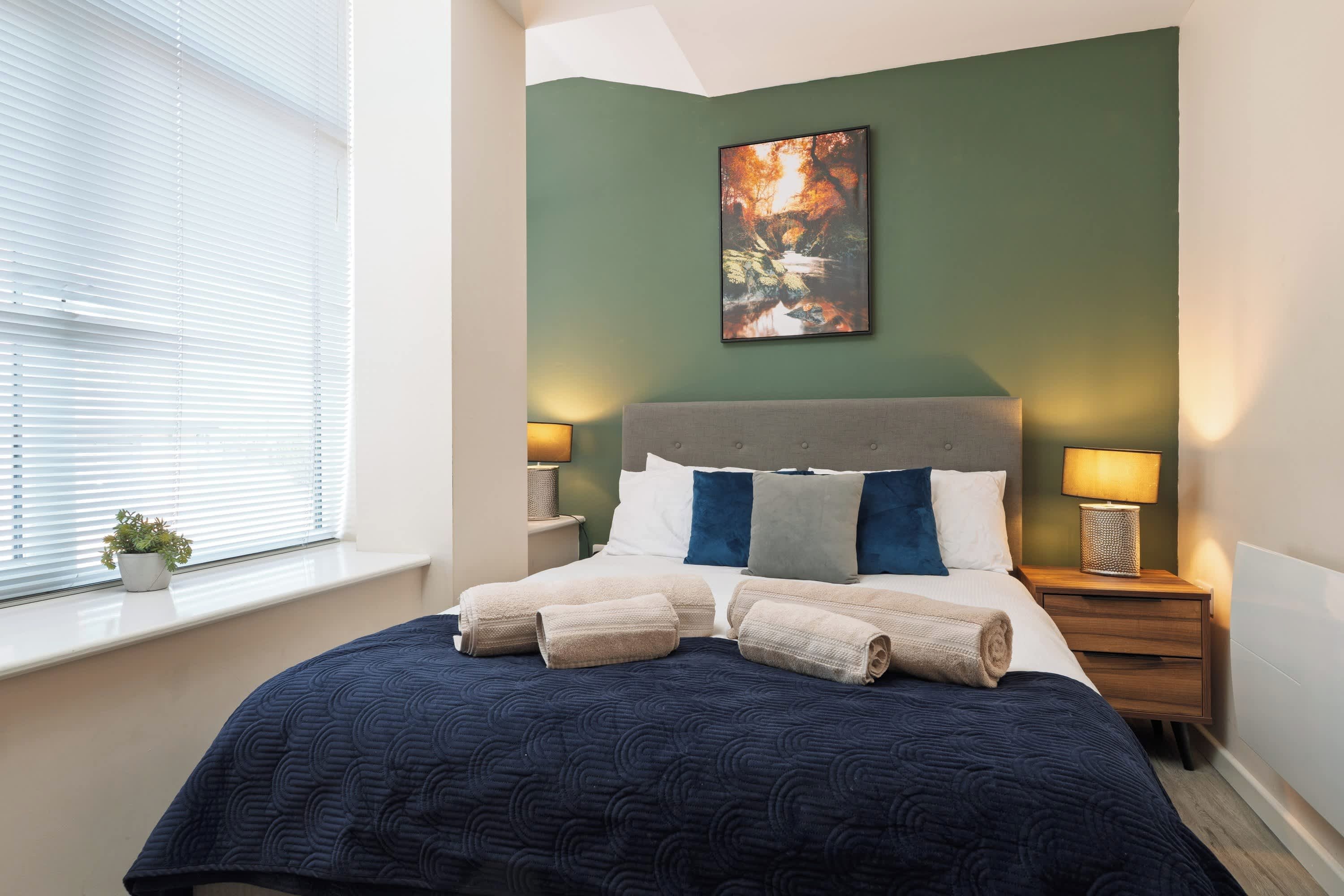 Une chambre à coucher avec un lit, des oreillers, une table de chevet, une lampe et un tableau au mur.