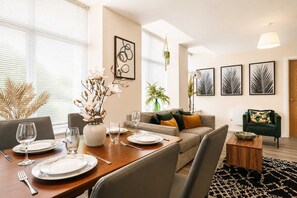 A modern living room with a dining area, featuring a sofa, coffee table, and decorative plants. - Stylish Salford Apartment | Free Parking (Manchester)