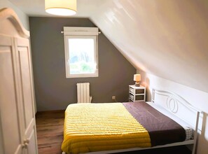 A bedroom with a bed, a nightstand, a window, a radiator, and a door.