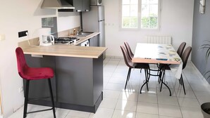 Eine moderne Küche mit einer zentralen Kochinsel, einem Esstisch mit Stühlen, einem roten Sessel und einem Fenster, das für natürliches Licht sorgt.
