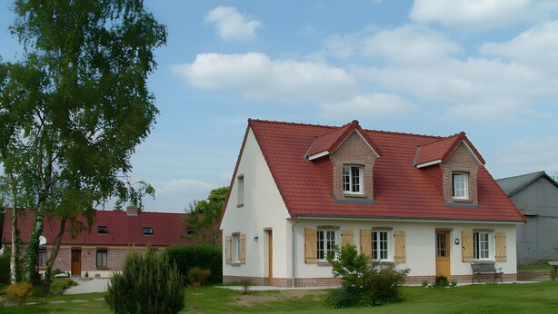 Ein zweistöckiges Haus mit rotem Dach, einer kleinen Veranda und einem gepflegten Rasen.