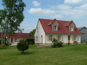 A two-story house with a red roof, a small front porch, and a well-maintained lawn.