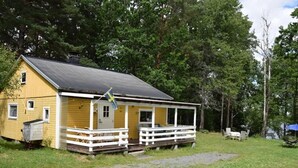 A yellow cabin with a porch, surrounded by trees. - Vacation home on the lake with rowing boat! (Nye)