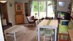 A cozy room with a wooden ceiling, a dining table with chairs, a television, and a window with curtains. - Vacation home on the lake with rowing boat! (Nye)