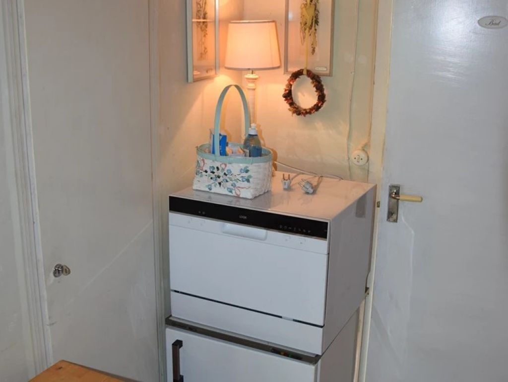 A compact kitchen with a dishwasher, a small countertop, and a wall-mounted lamp.