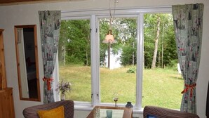 A room with two striped sofas, a wooden table, and a large window with curtains. - Vacation home on the lake with rowing boat! (Nye)