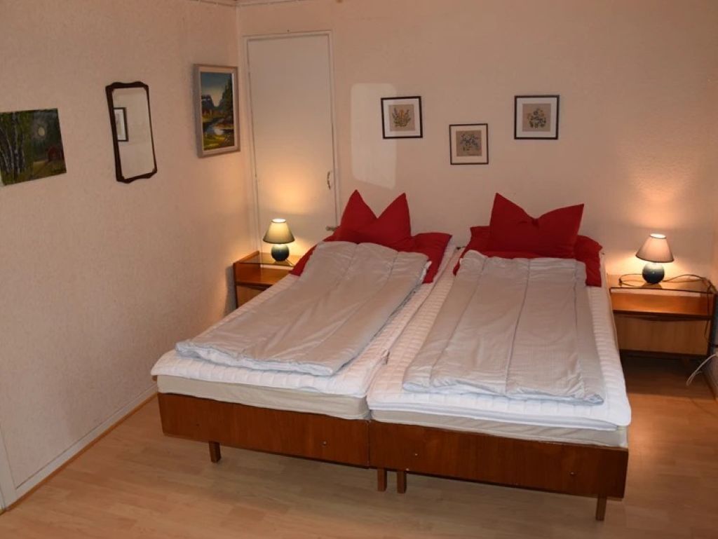 A double bed with red pillows, two bedside tables with lamps, and framed pictures on the walls.