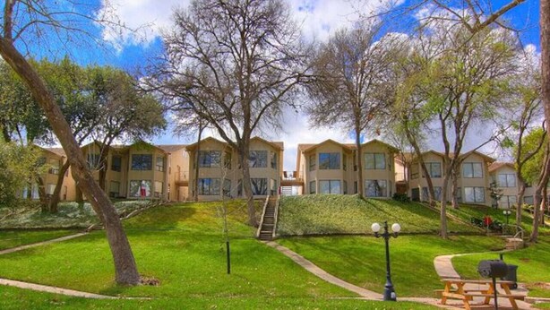 A residential building with multiple floors, a grassy courtyard, and a staircase leading to the entrance. - Comal River Condo 307 (New Braunfels)
