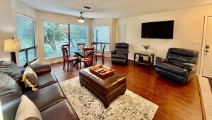A living room with a sofa, ottoman, chairs, a TV, and a fireplace. - Comal River Condo 307 (New Braunfels)