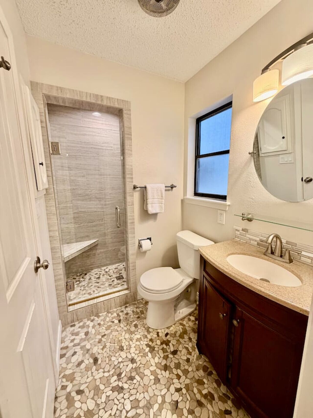 A bathroom with a shower, toilet, sink, and a window.