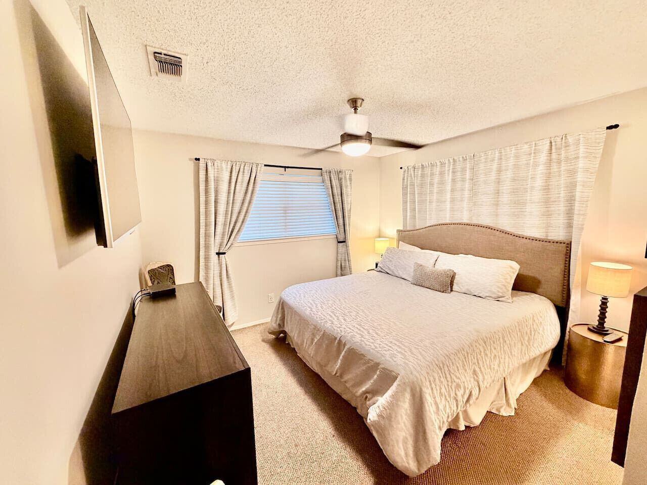 Une chambre d’hôtel avec un lit, un bureau, un ventilateur de plafond et une fenêtre avec des rideaux.