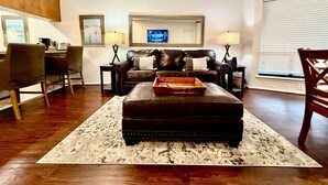 A living room with a leather sofa, ottoman, and a flat-screen TV on the wall. - Comal River Condo 307 (New Braunfels)