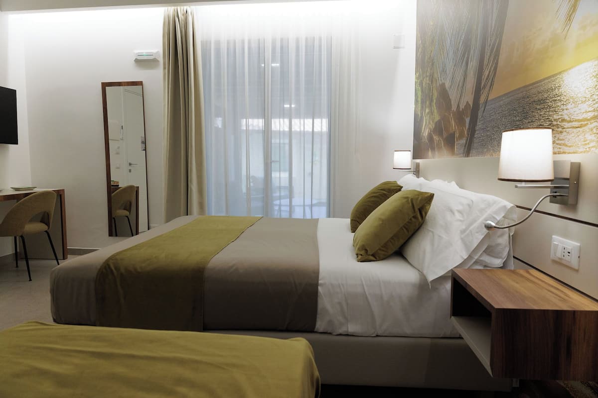 A hotel room with a bed, bedside table, lamp, and a large window with curtains.