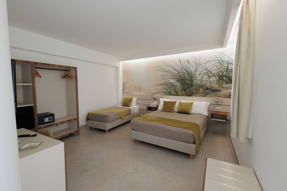 A bedroom with two beds, a wardrobe, a desk, and a plant.