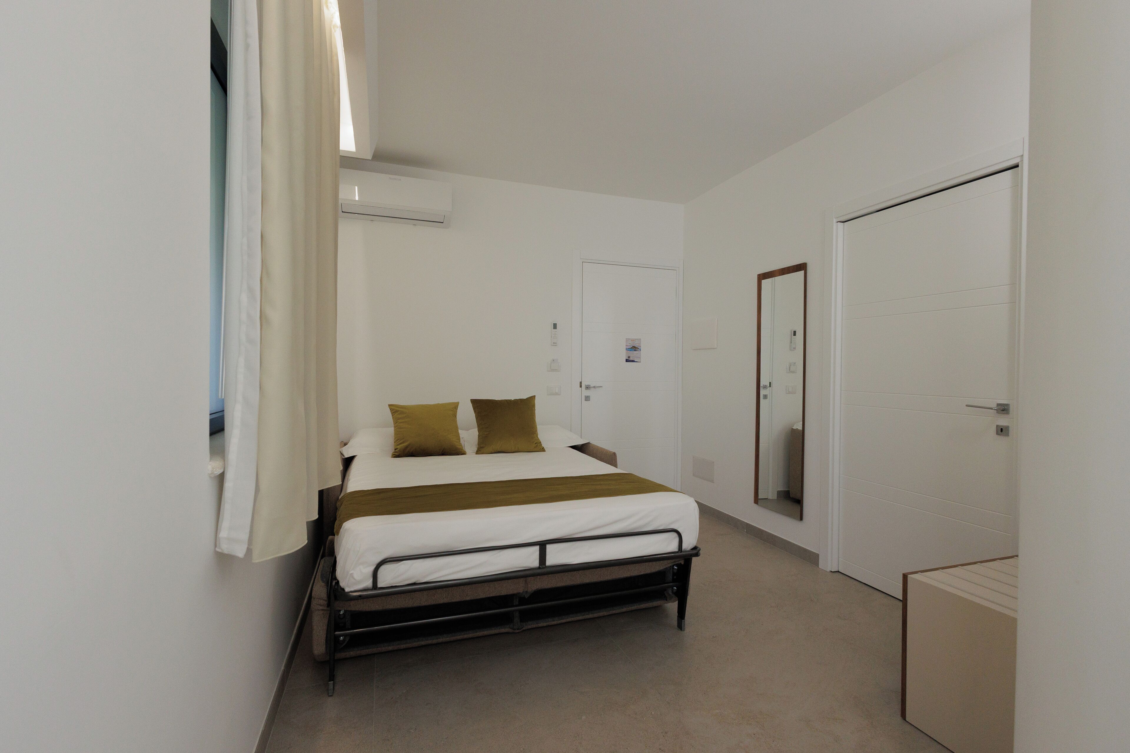A bedroom with a bed, a wardrobe, a mirror, and an air conditioning unit.