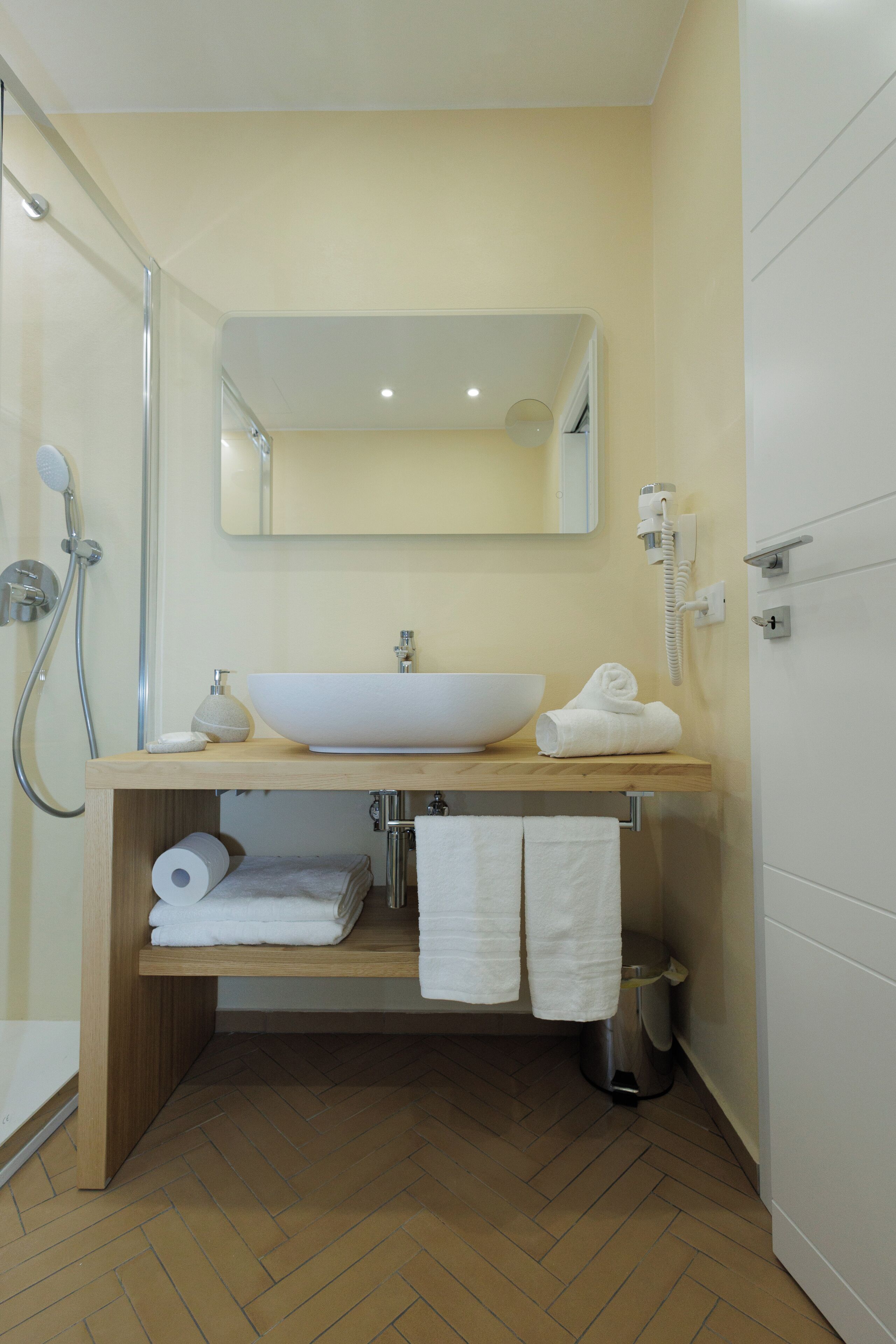 Un bagno con un mobile contenitore in legno, un lavabo bianco, uno specchio, una doccia e un water.