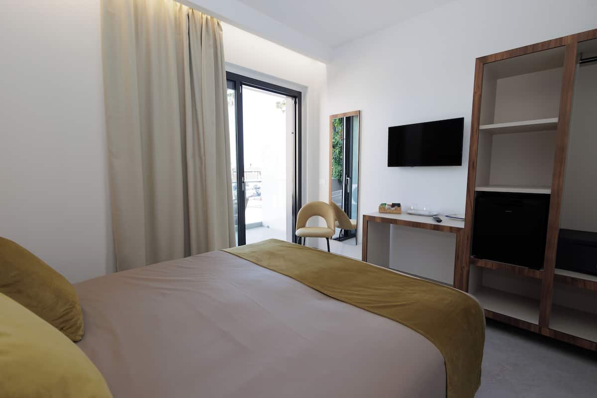 A hotel room with a bed, a desk with a TV, a chair, and a wardrobe.
