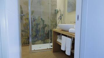 Een badkamer met een glazen douchecabine, een houten vloer, een witte wastafel en een spiegel.